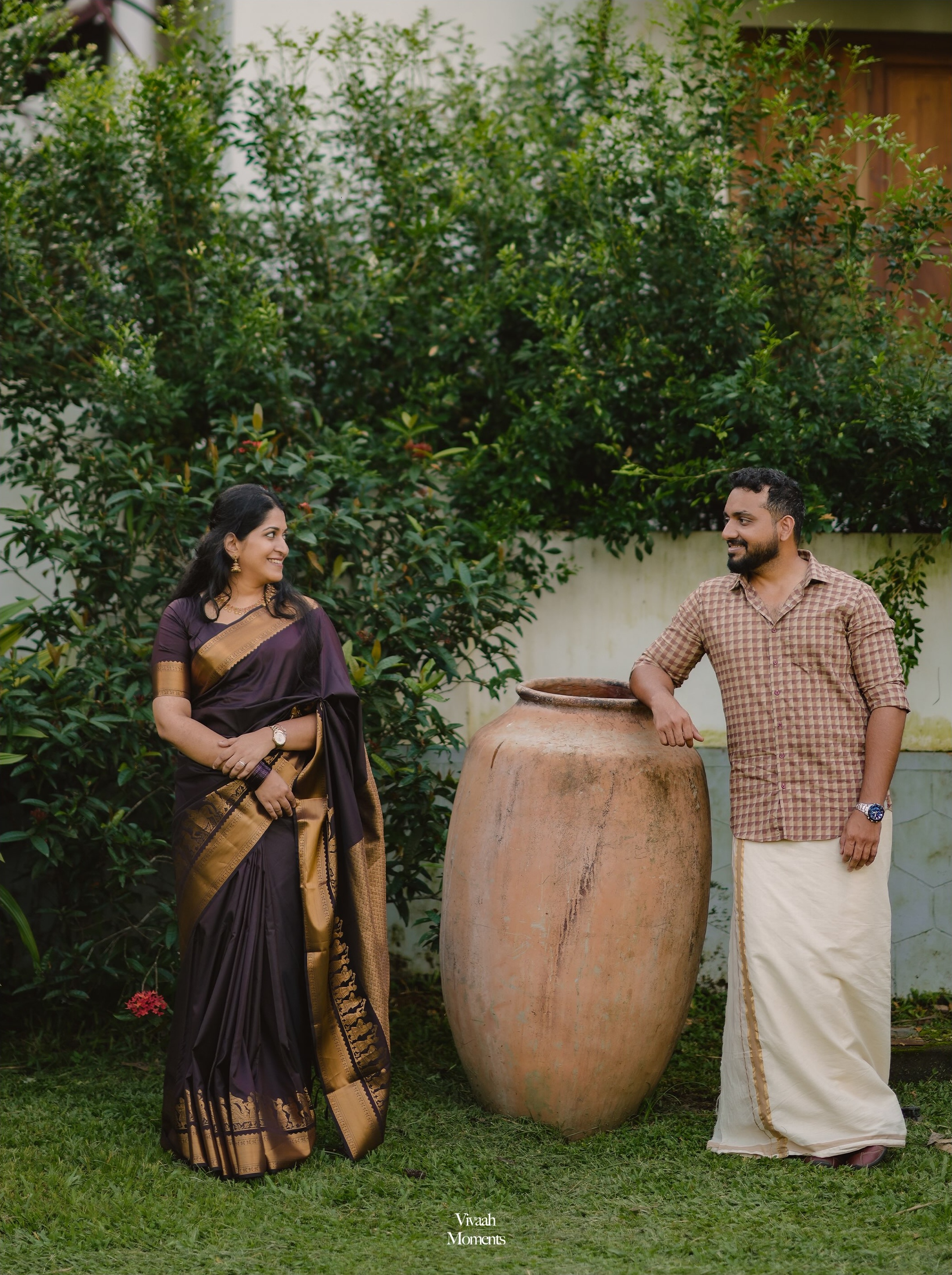 A couple in traditional attire standing beside a clay vessel